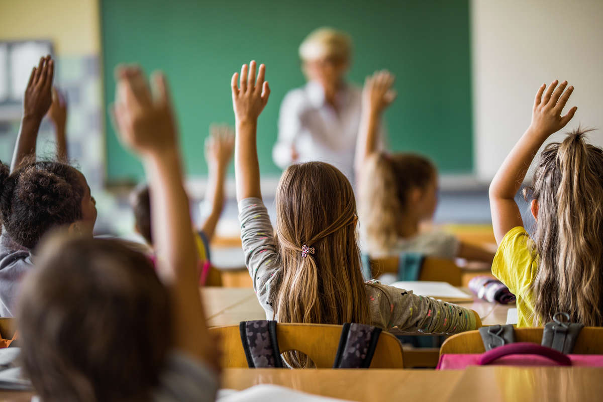 Canadian schools themed stock photo. Students with raised hands facing the teacher in front of the class.