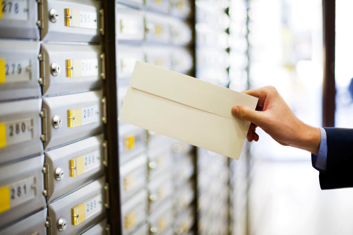 Mailing campaign themed stock photo. A business shirt and suit clad hand holding an envelope in front of a wall of mailboxes.